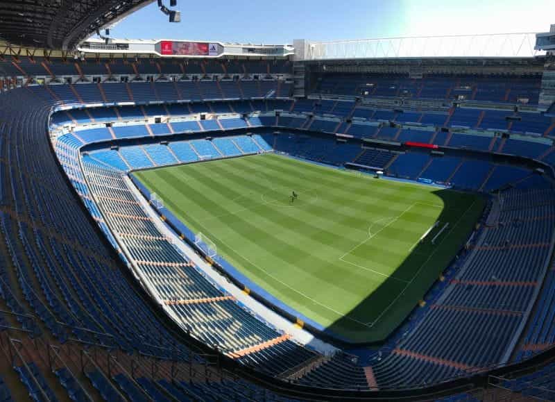 A green football pitch with empty stadium seating.