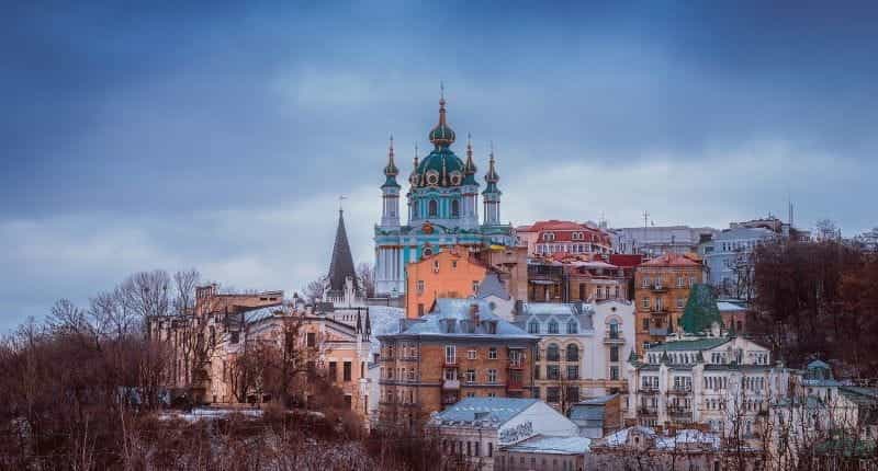 A Christian Orthodox church resting upon a hill in the Ukrainian capital city of Kiev, surrounded by colorful buildings.