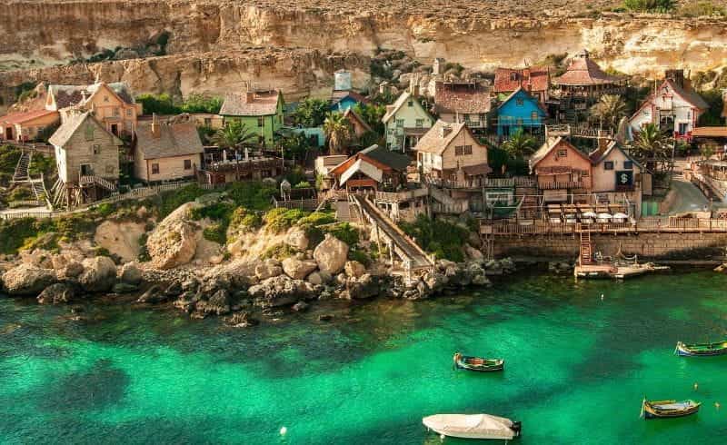 A rural costal Maltese fishing village, populated by small shacks and houses and numerous boats.