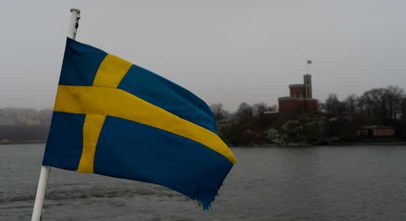 A flag of Sweden with a river and grey skies in the background.