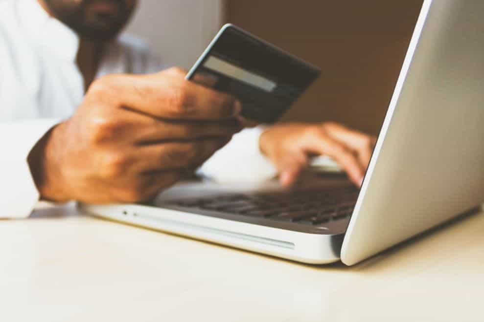 A man looking at his credit card as he completes a transaction on his laptop.