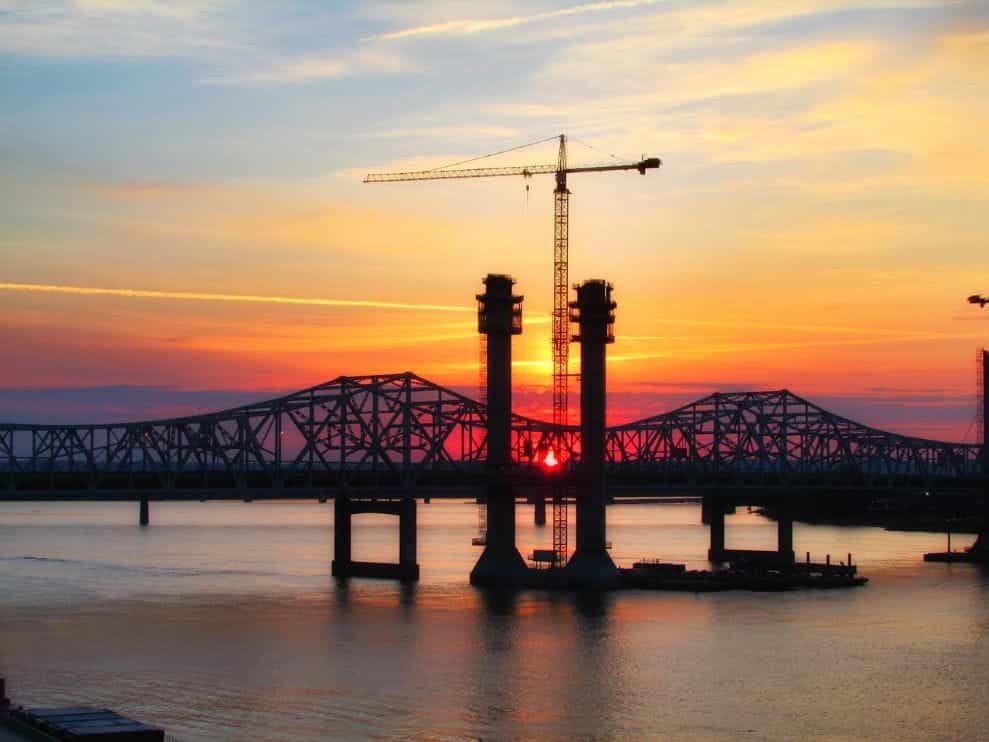 A large steel bridge during sunset, with a tall crane towering above it.