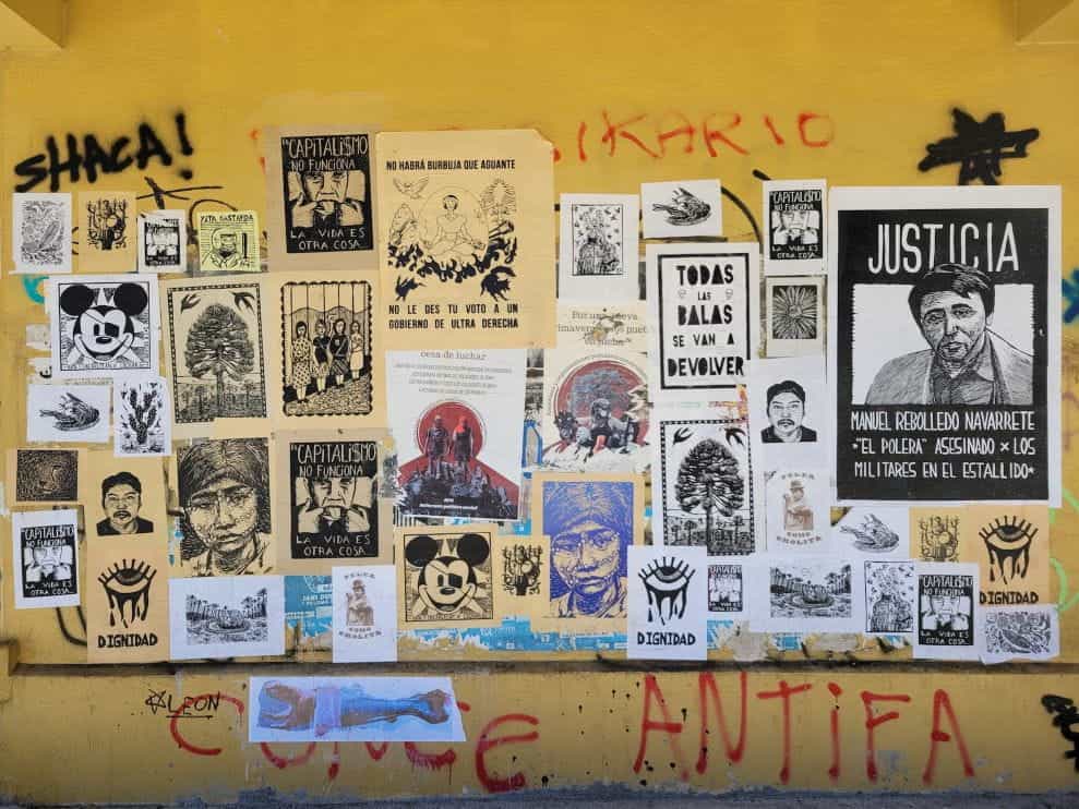 Various posters and graffiti on a yellow wall in Concepción, Chile.