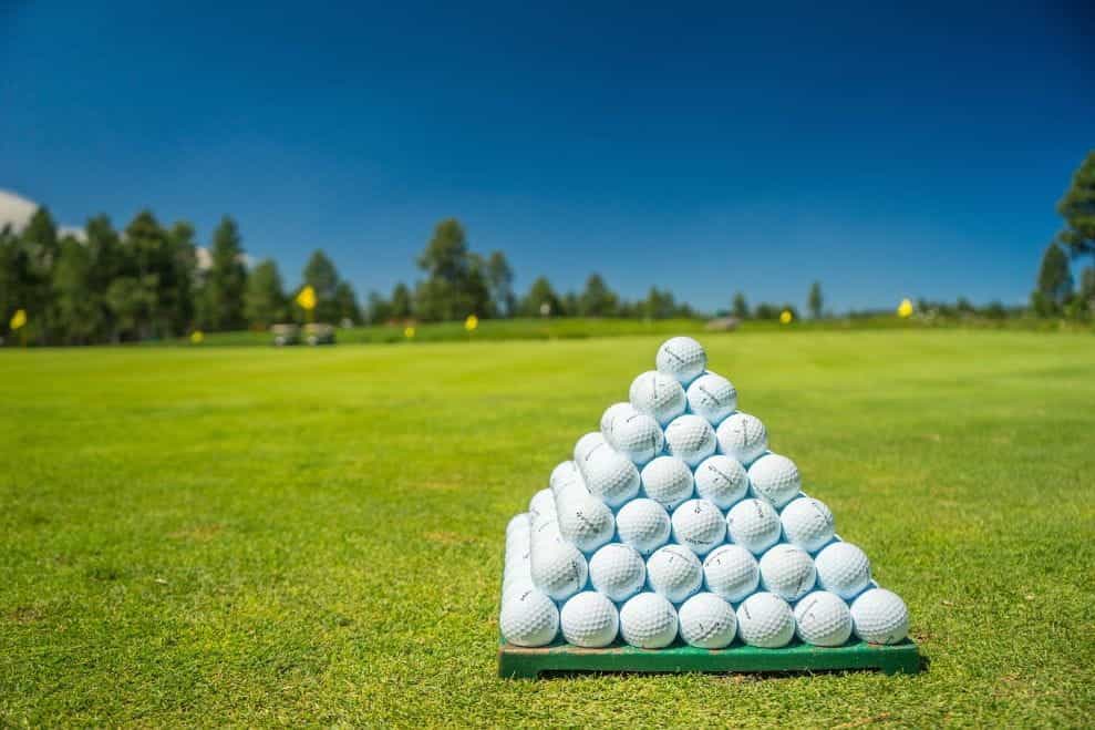 A pyramid of stacked golf balls resting on a golf green outdoors.