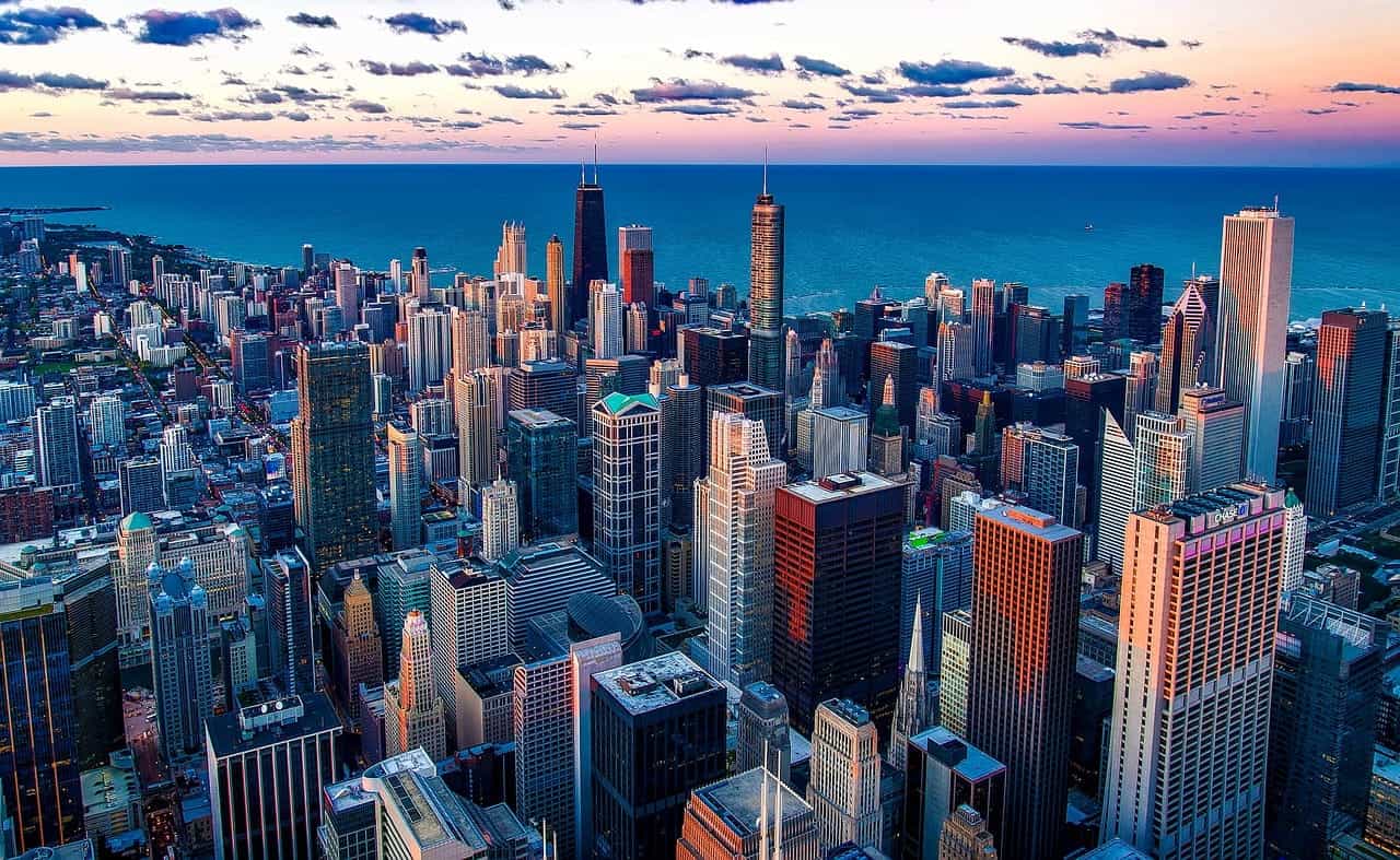 The dense downtown area of Chicago, Illinois, filled with skyscrapers and high-rise buildings, with Lake Michigan extending out to the horizon in the background.