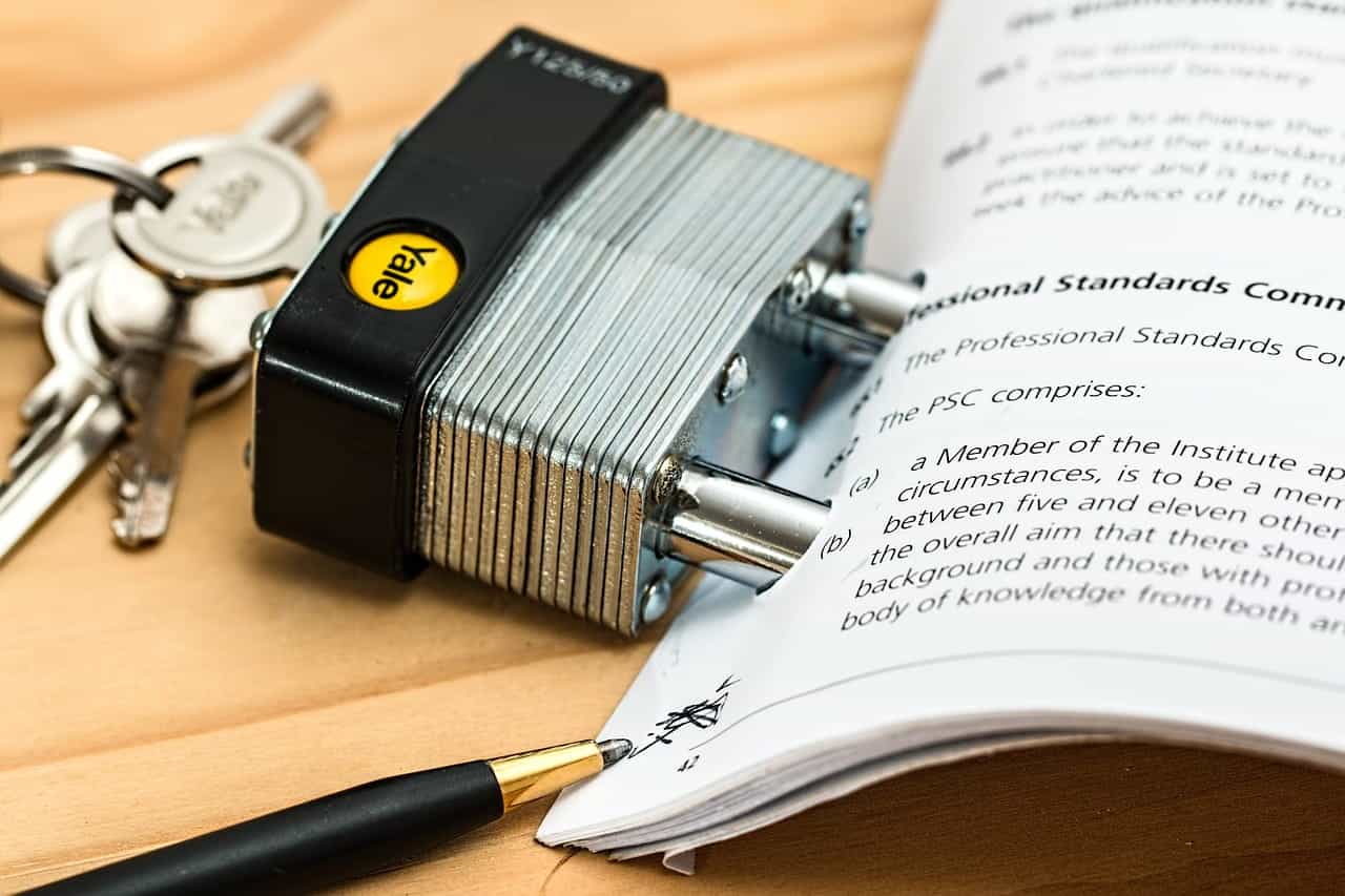 A padlock with the keys in it going through holes in the margin of a binding paper contract agreement, with a pen touching the corner of the document.