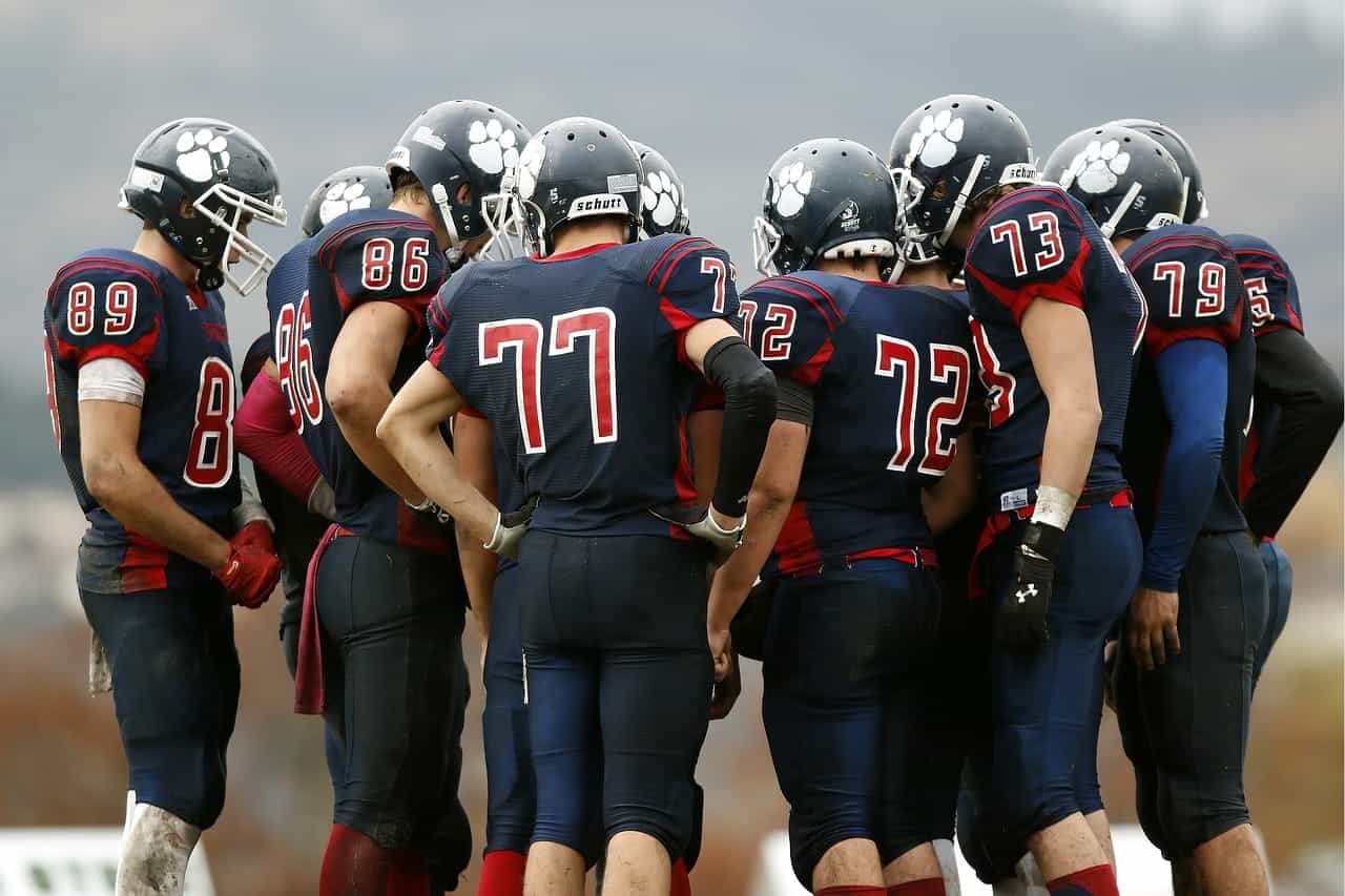 A team of American football players in full uniform huddled in a circle to discuss tactics before the start of a game.