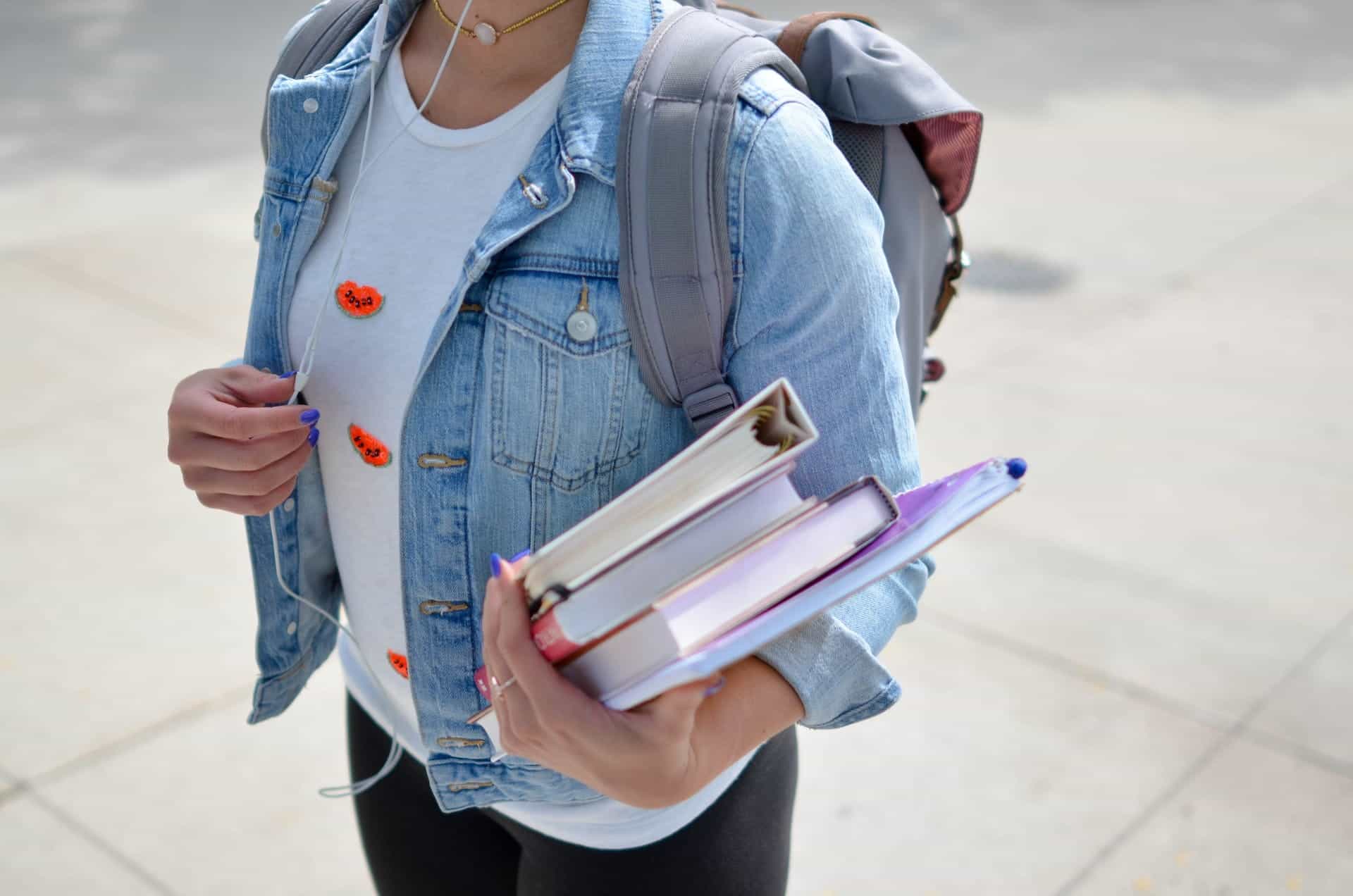 A young woman wearing a backpack holds school books.