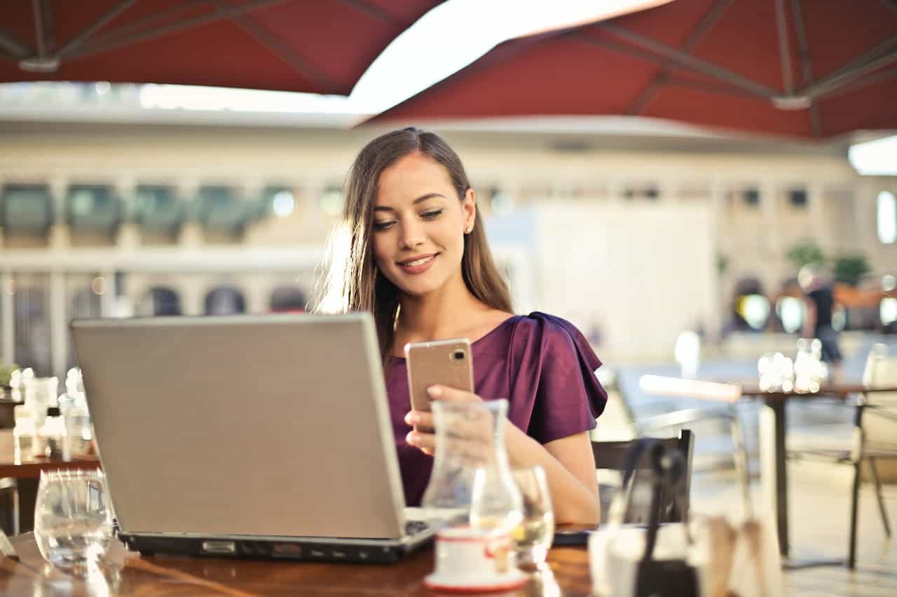 A woman with a laptop and cellphone at a café.