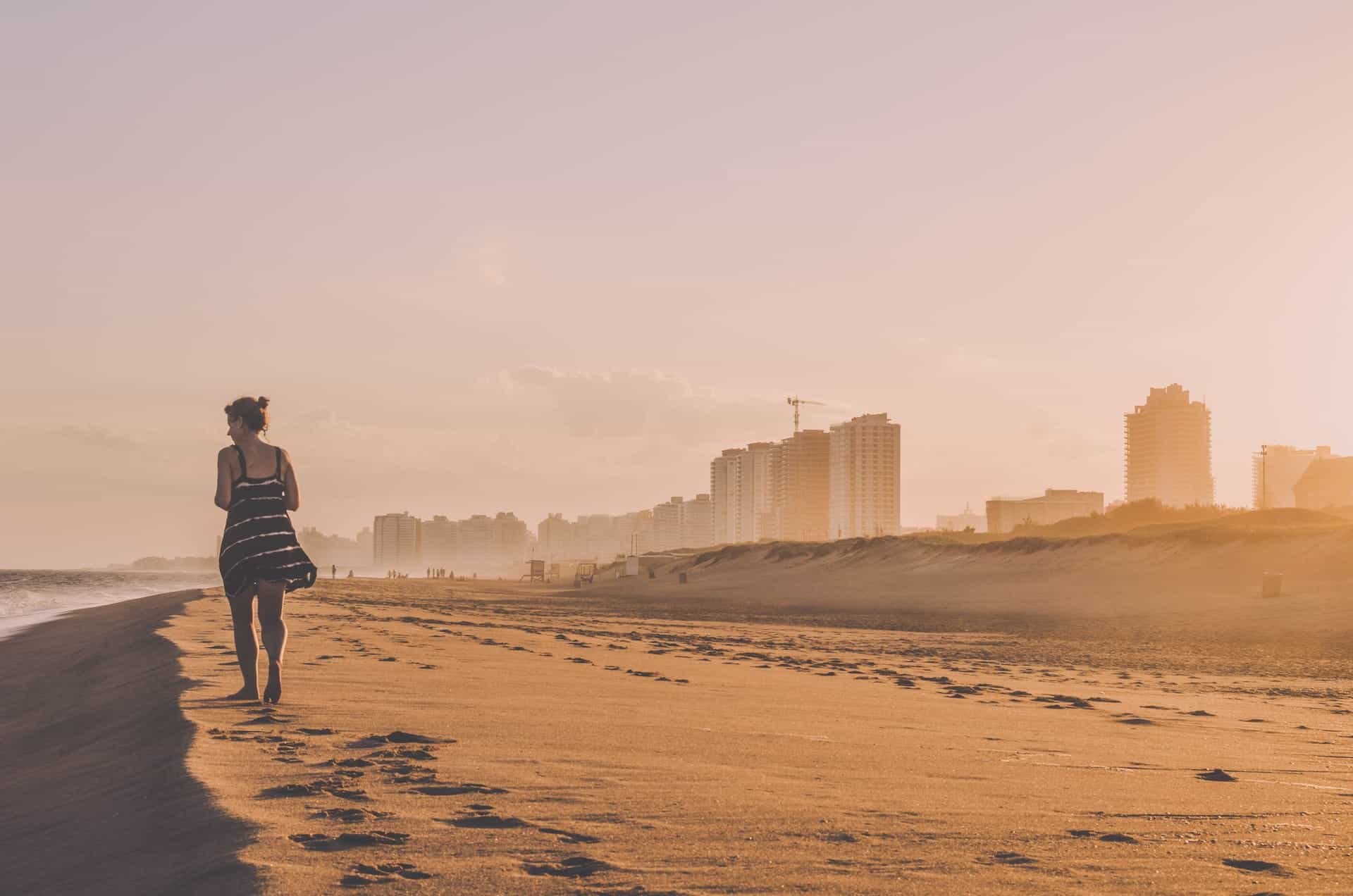 A woman walking on the beach at dusk, with buildings in the distance, in Punta del Este, Uruguay.