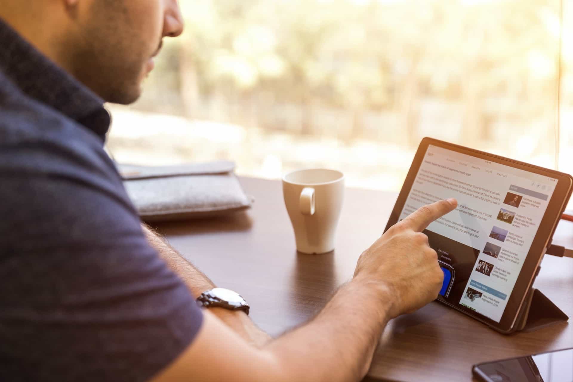 A man points at text on an internet website on a tablet screen, while sitting at a desk.