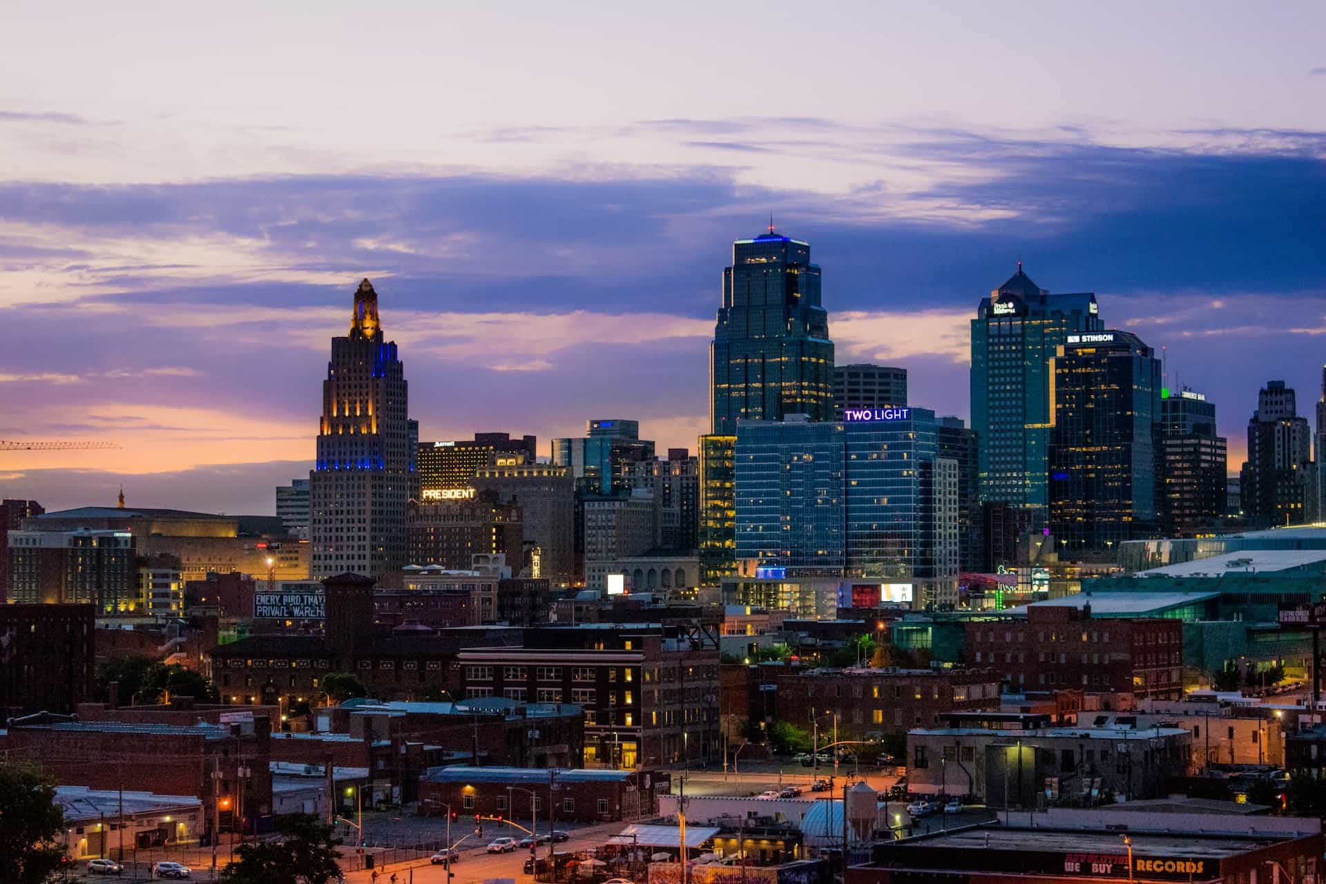 The skyline of downtown Kansas City, Missouri, showcasing numerous skyscrapers and tall buildings against a gradually darkening sky.