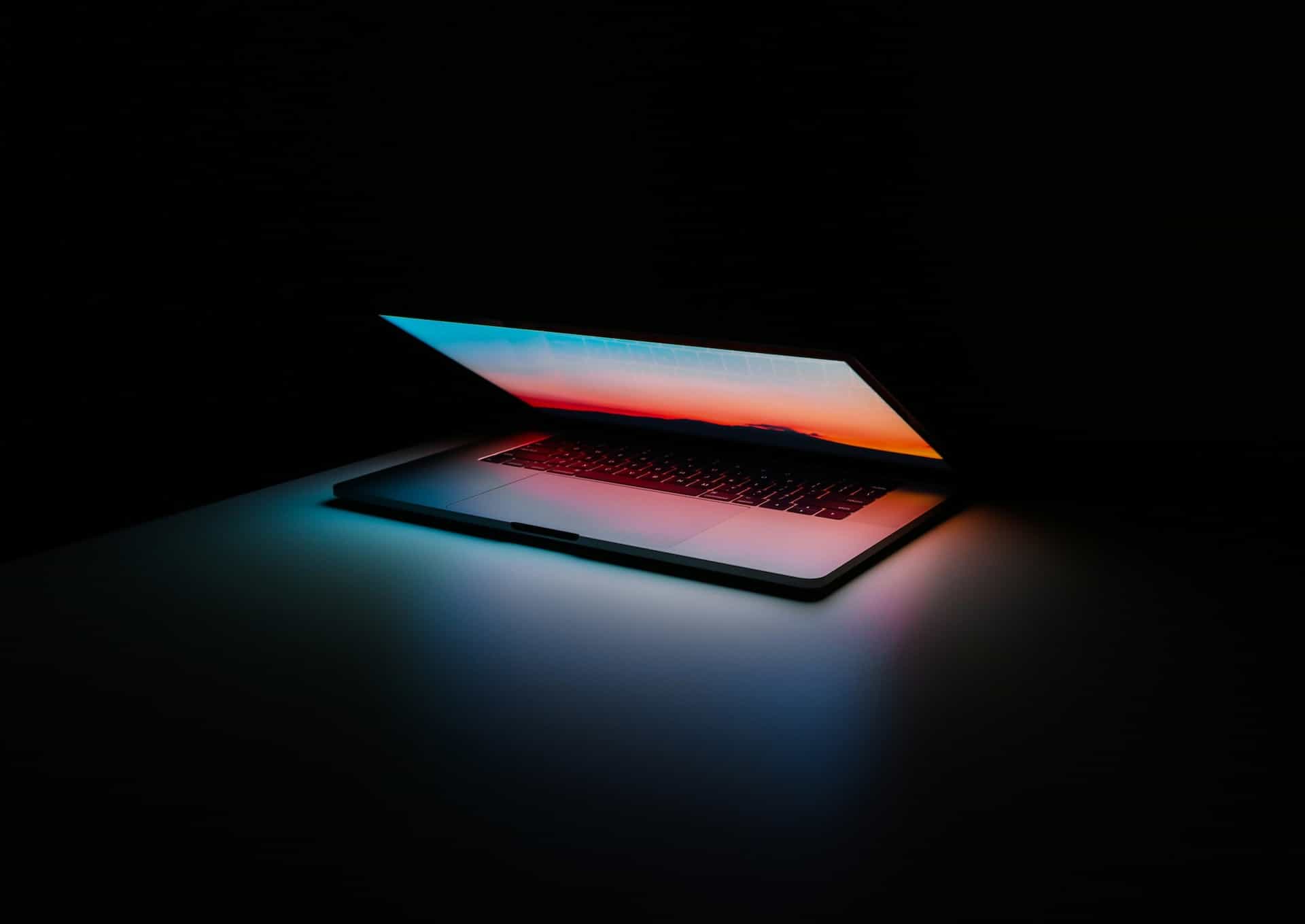 A laptop computer sitting on a table with the screen slightly lifted up, beaming down a warm orange light onto the device’s keyboard.