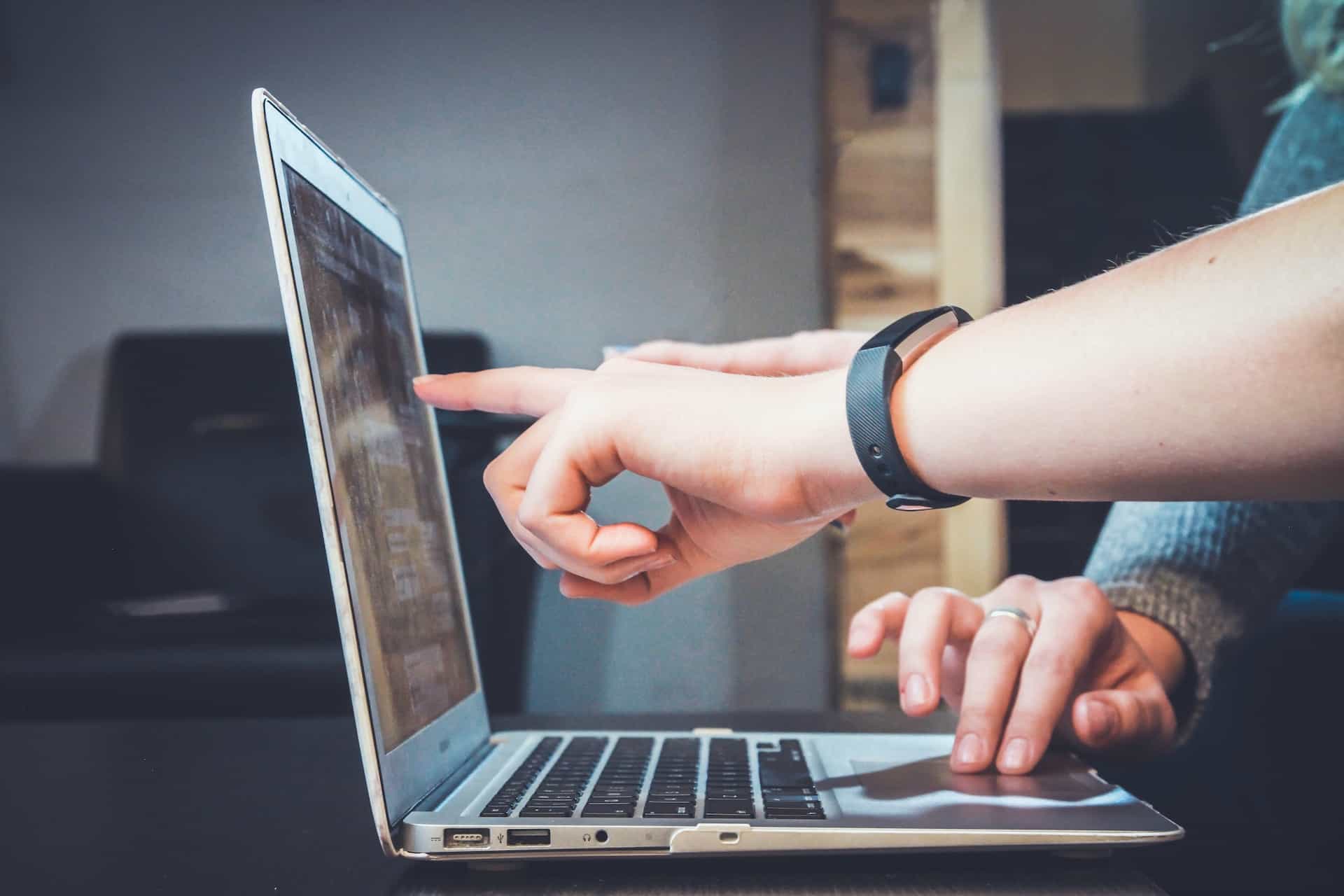 Two people pointing fingers at a laptop screen.